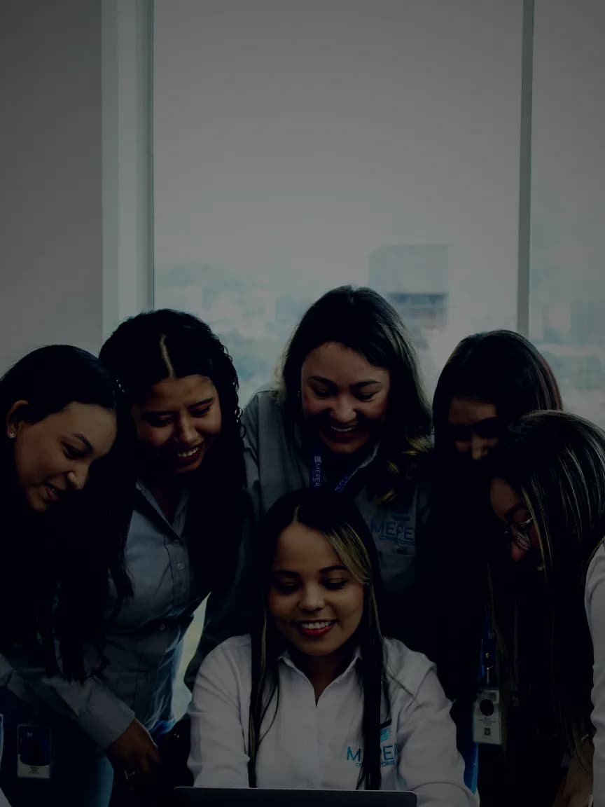 Seis consultoras de MEPER, con polo de marca, se agrupan sonrientes alrededor de un portátil sobre la mesa de juntas