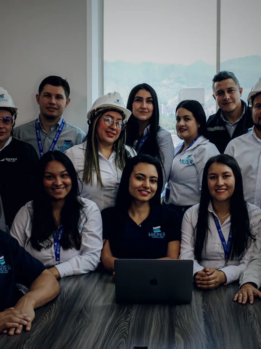 Equipo completo de MEPER Consultores reunido en sala de juntas, con la cordillera de Medellín al fondo