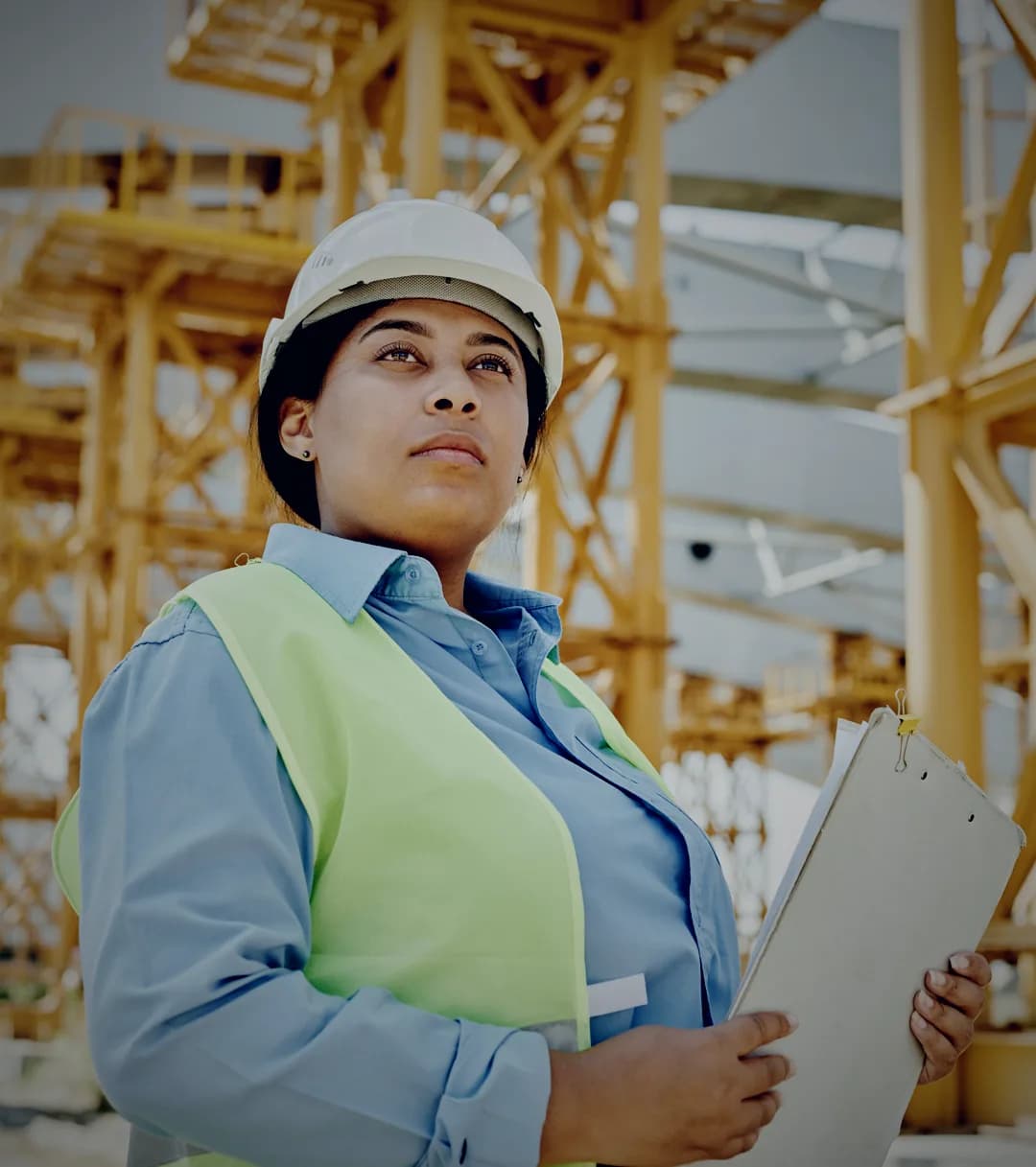 Ingeniera con casco y chaleco reflectivo revisando una estructura industrial, tablilla de inspección en mano